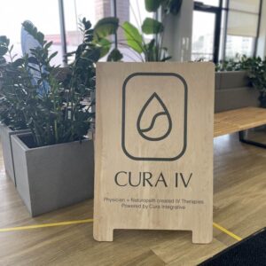 cura iv wooden sandwich board with logo with grey planters and plants in the background